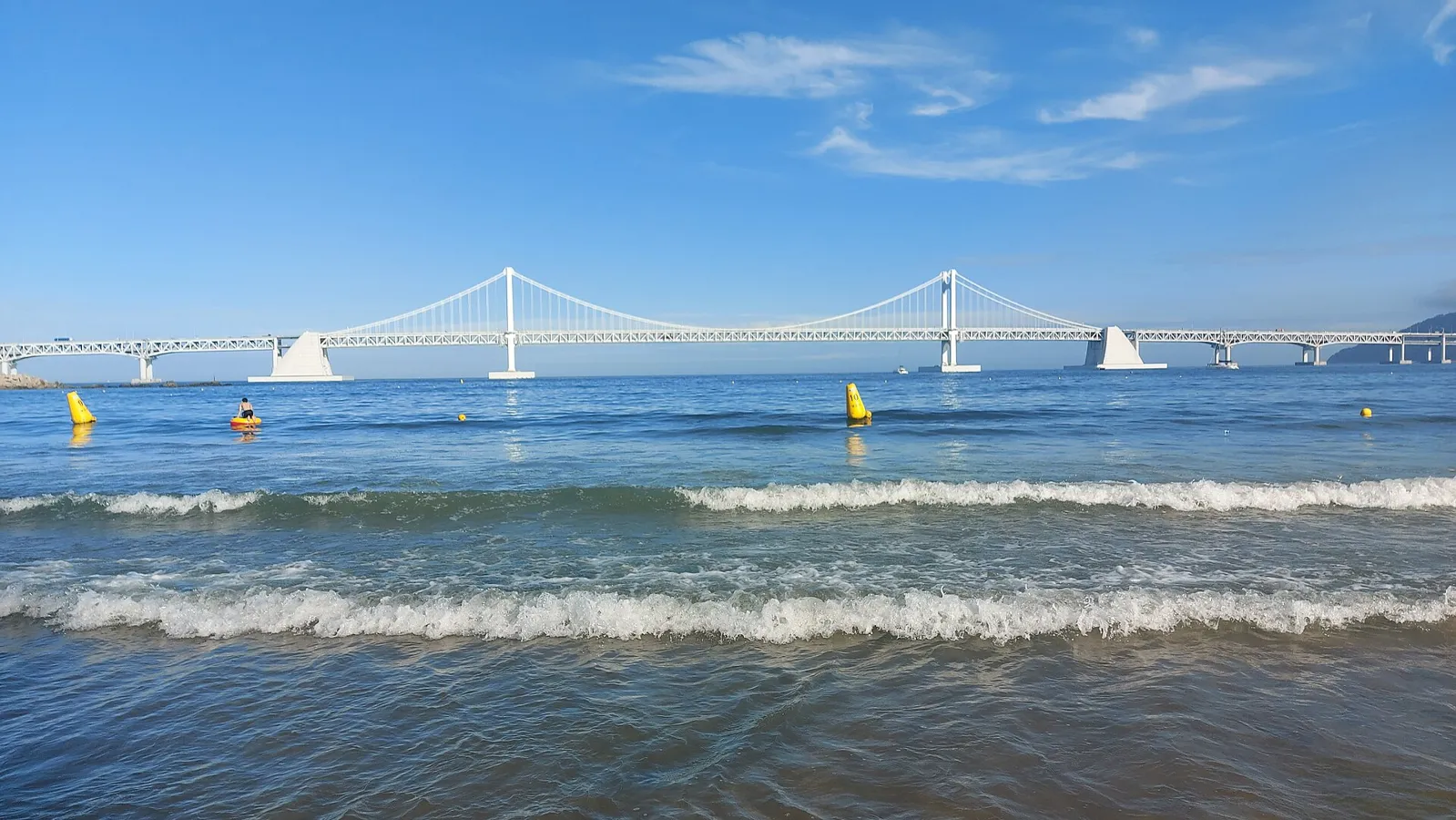 Waves on Gwangalli Beach with the white Gwangan suspension bridge across the bay