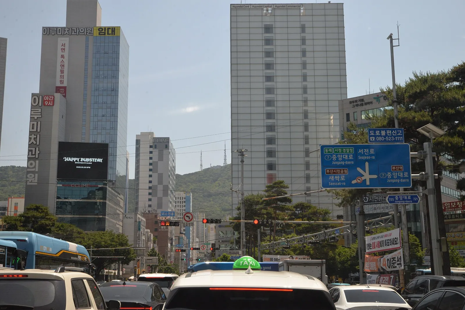 Traffic, taxis and a bus at the Seomyeon junction in Busan, with office towers and wooded hills behind