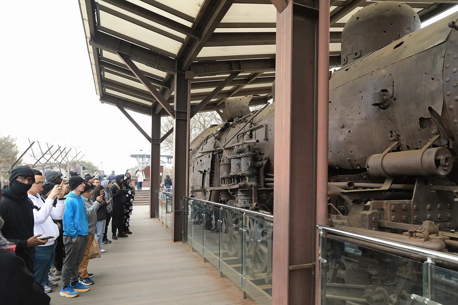 Visitors on a covered walkway beside a rusted, bullet-scarred steam locomotive at Imjingak