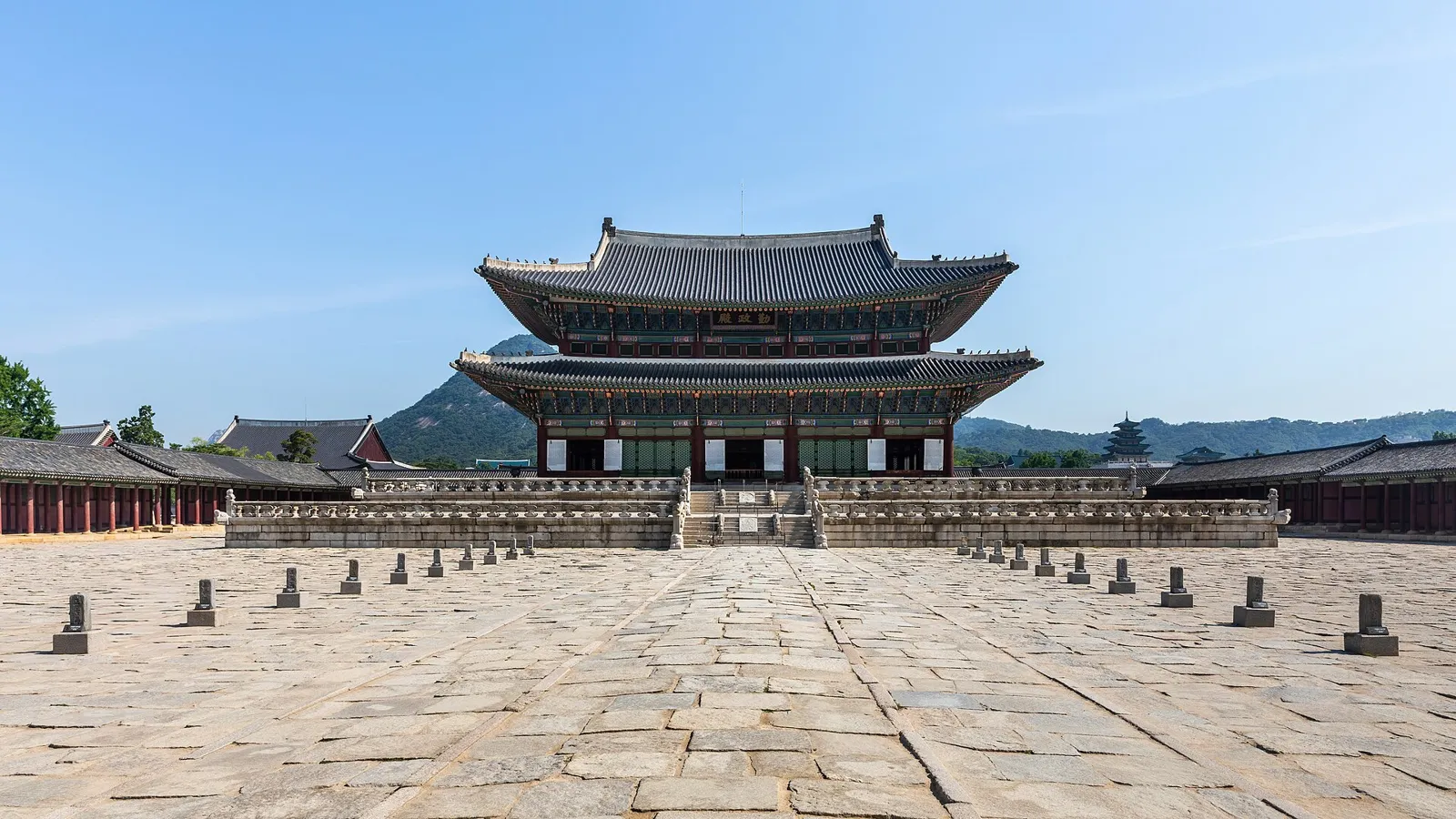 Geunjeongjeon, the palace's two-storey throne hall, across a wide stone courtyard under a blue sky