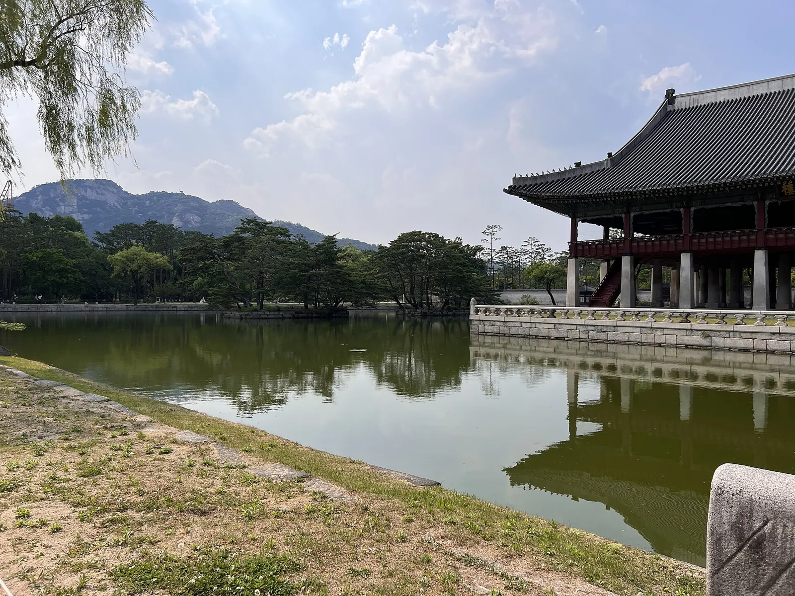 Gyeonghoeru pavilion beside a still pond, with the mountains north of Seoul behind it