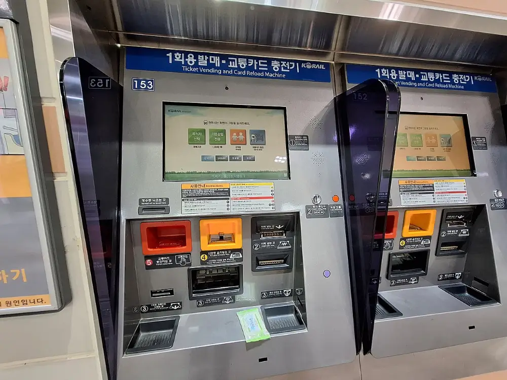 Two ticket vending and card reload machines in a Korean subway station, with screens and slots for cash and cards